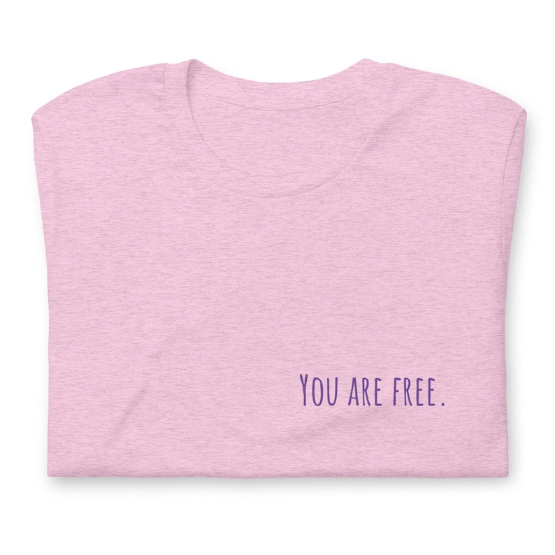 May include: A pink heather t-shirt with the text "YOU ARE FREE." printed in purple on the bottom right corner.