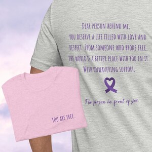 May include: Two t-shirts with a message of support and empowerment. The grey t-shirt has the text "DEAR PERSON BEHIND ME, YOU DESERVE A LIFE FILLED WITH LOVE AND RESPECT. FROM SOMEONE WHO BROKE FREE, THE WORLD IS A BETTER PLACE WITH YOU IN IT. WITH UNWAVERING SUPPORT, The person in front of you." The pink t-shirt has the text "YOU ARE FREE."