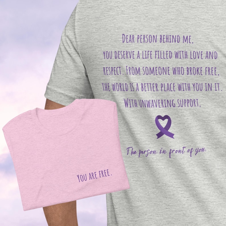 May include: Two t-shirts with a message of support and empowerment. The grey t-shirt has the text "DEAR PERSON BEHIND ME, YOU DESERVE A LIFE FILLED WITH LOVE AND RESPECT. FROM SOMEONE WHO BROKE FREE, THE WORLD IS A BETTER PLACE WITH YOU IN IT. WITH UNWAVERING SUPPORT, The person in front of you." The pink t-shirt has the text "YOU ARE FREE."