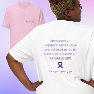May include: White t-shirt with a purple ribbon and the text "Dear person behind me, you deserve a life filled with love and respect. From someone who broke free. The world is a better place with you in it. With unwavering support, The person in front of you."