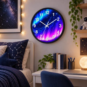 Pode incluir: Um relógio de parede redondo com moldura preta e um mostrador que exibe uma aurora boreal vibrante em tons de azul, roxo e rosa contra um céu estrelado. O relógio possui números brancos de 1 a 12 e ponteiros brancos de horas e minutos.