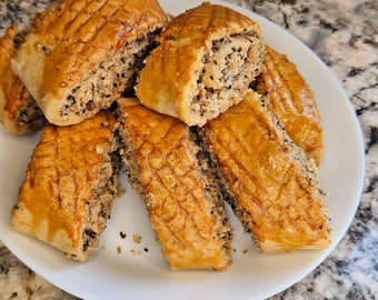 May include: A plate of golden brown pastries filled with a mixture of nuts and seeds. The pastries are arranged in a pile on a white plate.