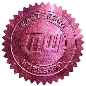 以下が含まれることがあります： メタリックピンクのシールで、星型の縁取りがあります。「MASTERSON WORKSHOP」の文字が周囲にあり、中央には様式化されたロゴがあります。ロゴは線と形の組み合わせのようです。