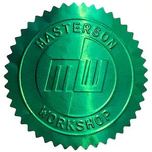 以下が含まれることがあります： 中央のロゴを囲む「MASTERSON WORKSHOP」の文字が入った、光沢のある緑色のシール。ロゴは3本の縦線と1本の横線で構成されています。シールはギザギザの星のような縁取りがされています。