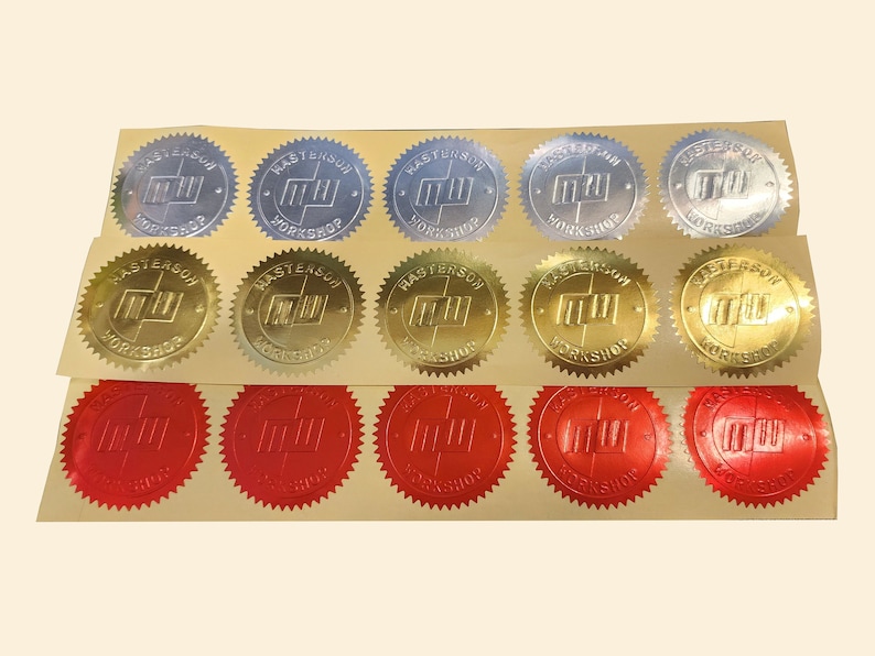 Sheets of shiny serrated circular stickers embossed with the Masterson Workshop seal in gold, silver, and red.