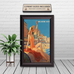 Puede incluir: Póster de viaje vintage enmarcado de Atlantic City. La obra de arte representa a una mujer con un traje de baño y sombrero naranja, sentada en una roca, con la ciudad y la playa al fondo. El póster está en un marco marrón oscuro.
