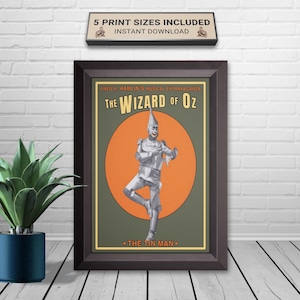 May include: A framed poster featuring The Wizard of Oz Tin Man character in a silver suit against a large orange circle and olive green background. The text reads The Wizard of Oz and The Tin Man. Above the frame is a sign stating 5 PRINT SIZES INCLUDED INSTANT DOWNLOAD.