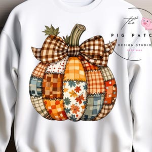 May include: White sweatshirt with a colourful patchwork pumpkin design, brown plaid bow and stem. The pumpkin is made of various fabric patterns, including leaves and plaid. The Pig Patch Design Studio logo is visible.
