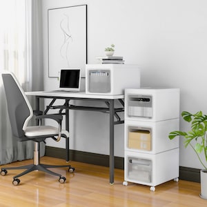 May include: White desk with a white office chair, a white desk lamp, and a white storage unit with three drawers. The storage unit has clear plastic drawers and is on wheels. The desk has a black metal frame and a white top. The chair has a black metal frame and a white seat.