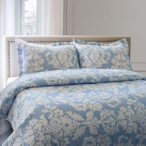 May include: A light blue quilted bedspread with a white damask pattern. The bedspread is on a bed with two matching pillowcases.