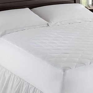 May include: A white quilted mattress pad with a fitted sheet. The pad is on a white bed with a white bed skirt.