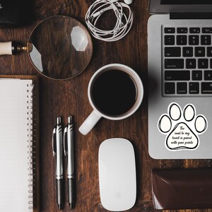 May include: A white laptop with a black paw print sticker on the trackpad. The sticker has the text "The road to my heart is paved with paw prints".