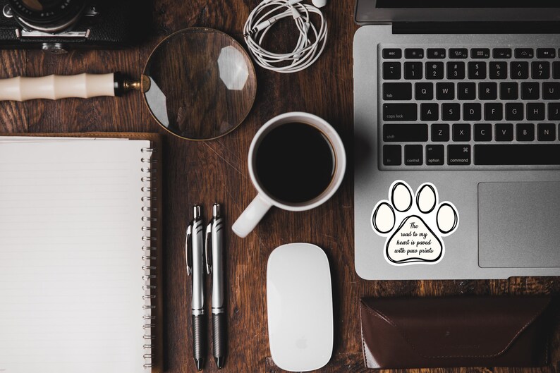 May include: A white laptop with a black paw print sticker on the trackpad. The sticker has the text "The road to my heart is paved with paw prints".