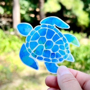 Könnte beinhalten: Ein blauer Aquarell-Schildkrötenaufkleber mit weißem Umriss. Die Schildkröte hat einen detaillierten Panzer mit einem strukturierten Muster.