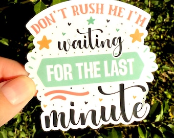 May include: A white sticker with the text "DON'T RUSH ME I'M waiting FOR THE LAST minute" in various fonts and colors. The sticker has a scalloped edge and is decorated with stars and hearts. The background is a blur of green leaves.