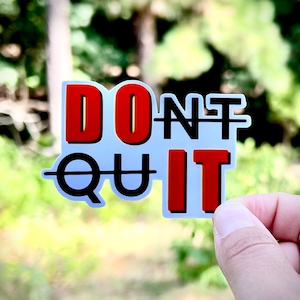 May include: White sticker with the words "DON'T QUIT" in black and red letters. The letters are outlined in black and the word "QUIT" is crossed out.