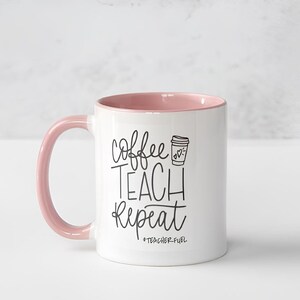 May include: White ceramic coffee mug with a pink rim and handle. The mug has black text that reads "coffee teach repeat" with a small coffee cup icon above the word "teach". The text "#teacherfuel" is below the words "repeat".