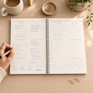 May include: A spiral-bound daily planner open to two pages with sections for top priorities, to-do lists, appointments, and health tracking. The left page is filled with handwritten notes in blue and red ink, including the date 12/05 and daily tasks.