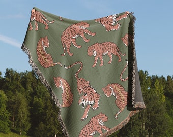 May include: A green woven throw blanket with a repeating pattern of orange tigers. The blanket has fringe on all sides.
