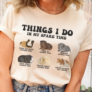 May include: A beige t-shirt with the text "Things I do in my spare time" and images of guinea pigs with text describing activities like "Hang out with guinea pigs", "Look at guinea pigs", "Research guinea pigs", "Talk about guinea pigs", "Dream about guinea pigs", and "Watch guinea pig videos".