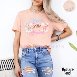 May include: A pink t-shirt with the text "Keeper of the Gender" in pink and blue lettering. Two teddy bears are holding balloons, one blue and one pink, and are floating on clouds with stars.