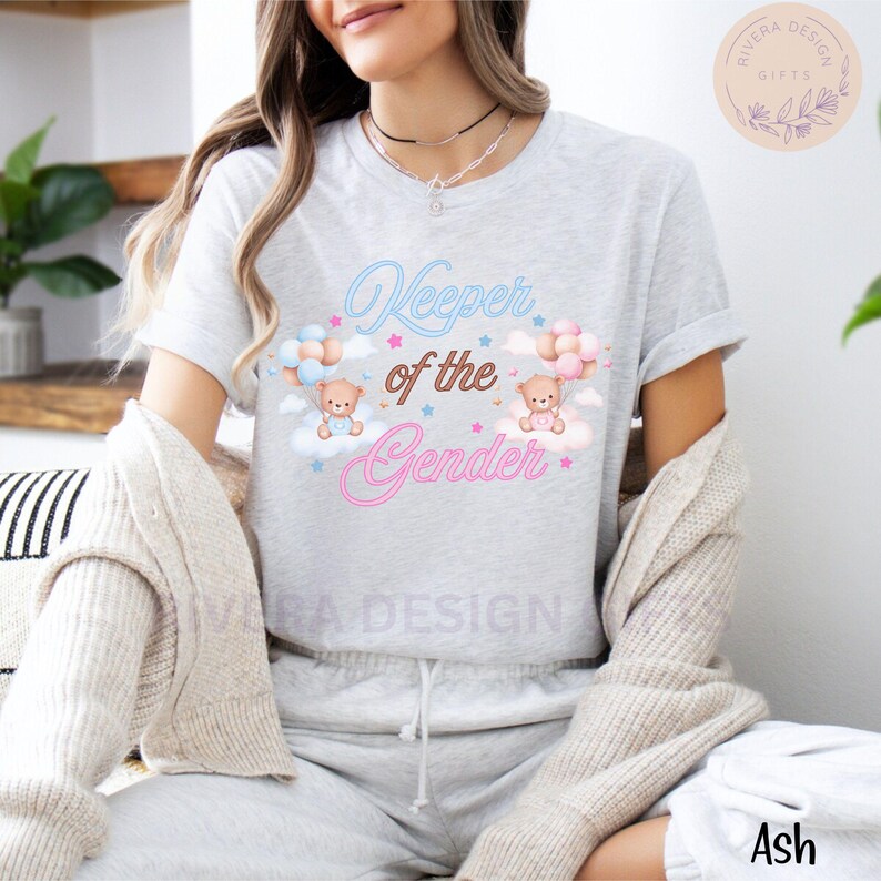May include: A gray t-shirt with the text "Keeper of the Gender" in pink and blue neon lettering. Two teddy bears are holding blue and pink balloons, floating above clouds with stars.