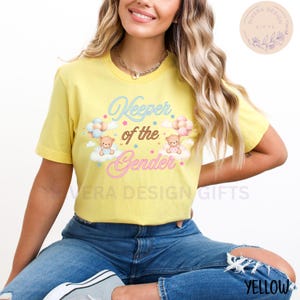 May include: A yellow t-shirt with the text "Keeper of the Gender" in brown and pink lettering. Two cartoon teddy bears are holding balloons, one blue and one pink, and are floating on clouds.