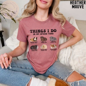 May include: A heather mauve t-shirt with the text "Things I do in my spare time" and a graphic of six guinea pigs with different activities. The activities include hanging out with guinea pigs, looking at guinea pigs, researching guinea pigs, talking about guinea pigs, dreaming about guinea pigs, and watching guinea pig videos.