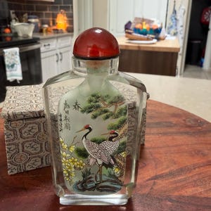 May include: A white ceramic mug with a black handle and the text "But First, Coffee" in a black, bold font. The mug is on a white surface. The mug is approximately 4 inches tall.