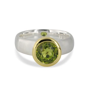 Könnte beinhalten: Ein silberner Ring mit einer goldenen Zargenfassung, in der ein grüner Peridot-Edelstein sitzt.