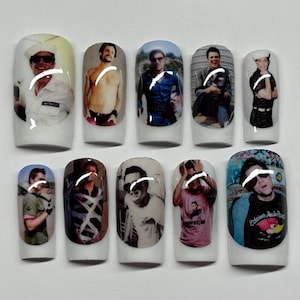 May include: A set of ten white press-on nails, each featuring a distinct photographic print of a person in various outfits and poses. The images include portraits of a person in a sailor hat, a shirtless person, and a person wearing graphic t-shirts.