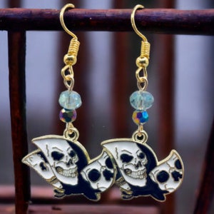 Puede incluir: Pendientes de aro dorados con un diseño de calavera en blanco y negro. Las calaveras llevan una capucha negra. Los pendientes tienen cuentas de cristal azul claro e iridiscente.