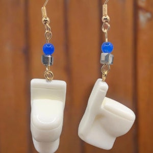 May include: A pair of gold earrings with blue and silver beads, each earring features a white ceramic toilet charm.