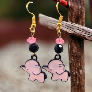 May include: A pair of dangle earrings featuring pink elephant charms, black beads, and pink and clear glass beads.