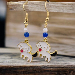 May include: Gold dangle earrings with white enamel dog charms, blue and white beads, and gold hooks.