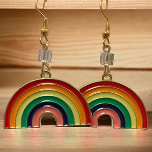 May include: A pair of rainbow-colored earrings with a gold hook and a clear crystal bead. The earrings are shaped like rainbows with red, orange, yellow, green, blue, indigo, and violet stripes.