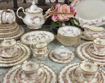 Könnte beinhalten: Eine Sammlung weißer Porzellanwaren mit rosa Rosenblütenmustern und goldenen Verzierungen. Das Set umfasst Tassen, Untertassen, Teller, Schalen, eine Teekanne, einen Sahnekännchen, eine Zuckerdose und eine Sauciere. Vintage-Geschirr.