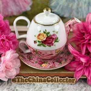 Puede incluir: Juego de té vintage con tetera, platillo y taza blancos, decorados con rosas rosas y amarillas. La tetera tiene un asa y tapa doradas. El platillo y la taza son rosas con un estampado floral a juego. TheChinaCollector está impreso en la parte inferior.