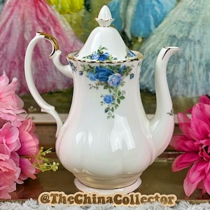 May include: White porcelain teapot with a lid, decorated with blue floral patterns and gold detailing. The teapot has a curved handle and spout. The base is a light beige colour. The China Collector is printed on the base.