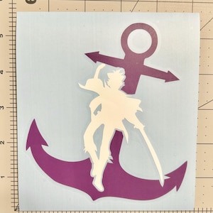 Puede incluir: Un adhesivo de vinilo morado con forma de ancla que presenta la silueta blanca de una figura pirata sosteniendo una espada, sobre un soporte azul claro con una regla visible que muestra medidas en cent&iacute;metros en los bordes izquierdo y superior.