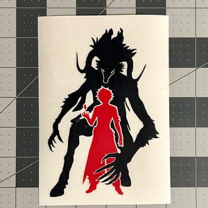 Puede incluir: Una calcoman&iacute;a de vinilo que presenta la silueta negra de una criatura con cuernos y garras detr&aacute;s de la silueta roja de una figura humana con cabello puntiagudo. El dise&ntilde;o se presenta sobre una hoja de respaldo rectangular de color blanco.