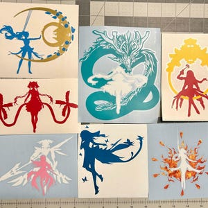 Puede incluir: Una colecci&oacute;n de siete pegatinas de vinilo con varias siluetas de estilo anime. Los dise&ntilde;os incluyen una figura azul con una luna creciente dorada, un drag&oacute;n verde azulado, un marco amarillo con una figura roja y otros personajes.