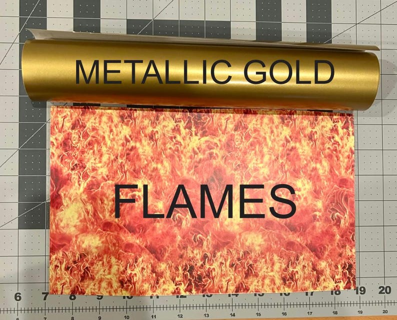 Puede incluir: Un rollo de vinilo adhesivo dorado met&aacute;lico colocado sobre una hoja rectangular con un estampado gr&aacute;fico vibrante y de alto contraste de llamas naranjas y amarillas. El texto METALLIC GOLD est&aacute; en el rollo y FLAMES en la hoja.