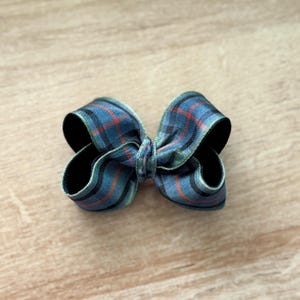 May include: A small, decorative bow made from plaid ribbon. The bow features a pattern of blue, green, and red lines on a dark background. The bow is tied in the center and has two loops on each side.