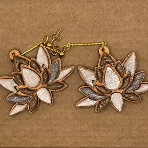Puede incluir: Un par de pendientes de madera con un diseño de flor de loto. Los pendientes están pintados en tonos de marrón, gris y blanco.