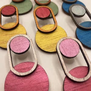 Puede incluir: Un conjunto de seis pares de pendientes de madera con formas geométricas. Los pendientes están hechos de madera y tienen una variedad de colores, incluyendo amarillo, verde, azul, rojo y rosa.