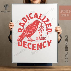 Puede incluir: Una impresión rectangular con un gráfico rojo de un cuervo que sostiene una pequeña rama en el pico. El texto RADICALIZED BY BASIC DECENCY está arqueado alrededor del ave en letras mayúsculas rojas, acentuado por pequeñas estrellas de cuatro puntas.