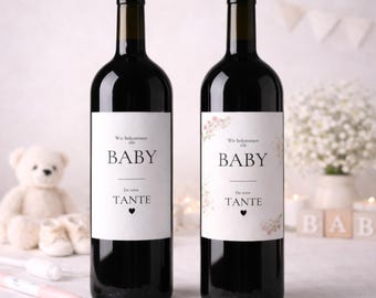 May include: Two dark glass wine bottles with white labels. The labels read "BABY" in large letters, with additional text above and below. One label has floral accents. The bottles are on a table with baby-themed decorations.