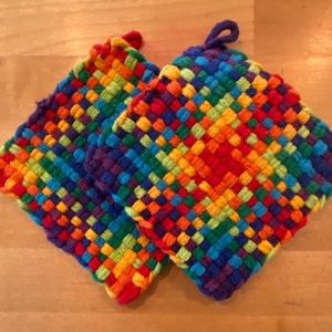 Peut inclure: Deux maniques tissées arc-en-ciel de forme carrée avec une surface texturée. Les maniques sont faites de fils colorés et ont un détail de frange.