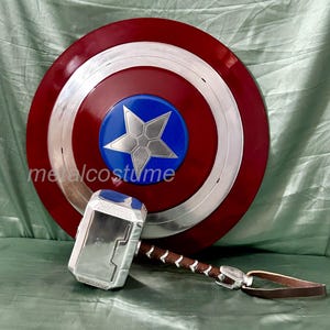 Op de afbeelding: Een rood, wit en blauw Captain America schild met een zilveren ster in het midden. Een zilveren en zwarte Thor's hamer met een bruine leren riem is op de voorgrond.